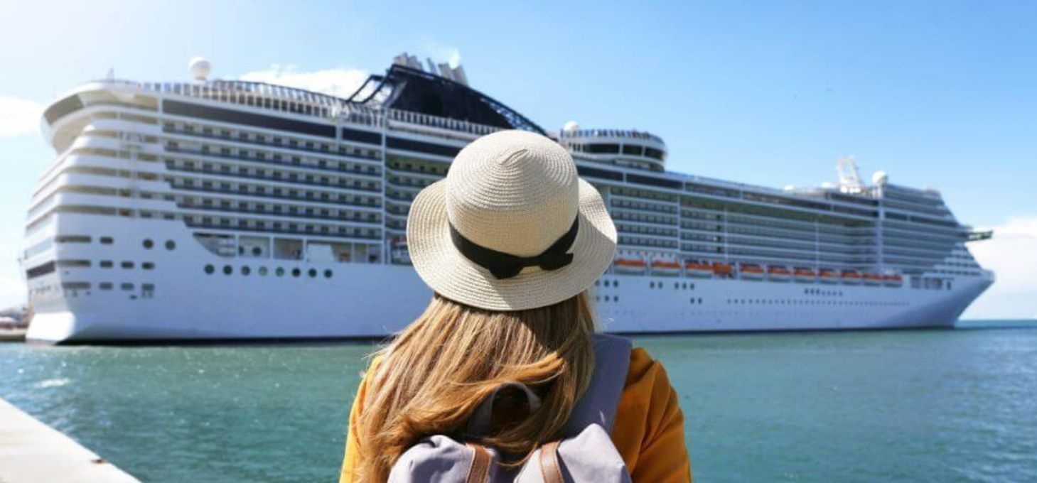 Woman in a straw hat with a cruise ship in the background. She faces away from the camera, on a sunny day.