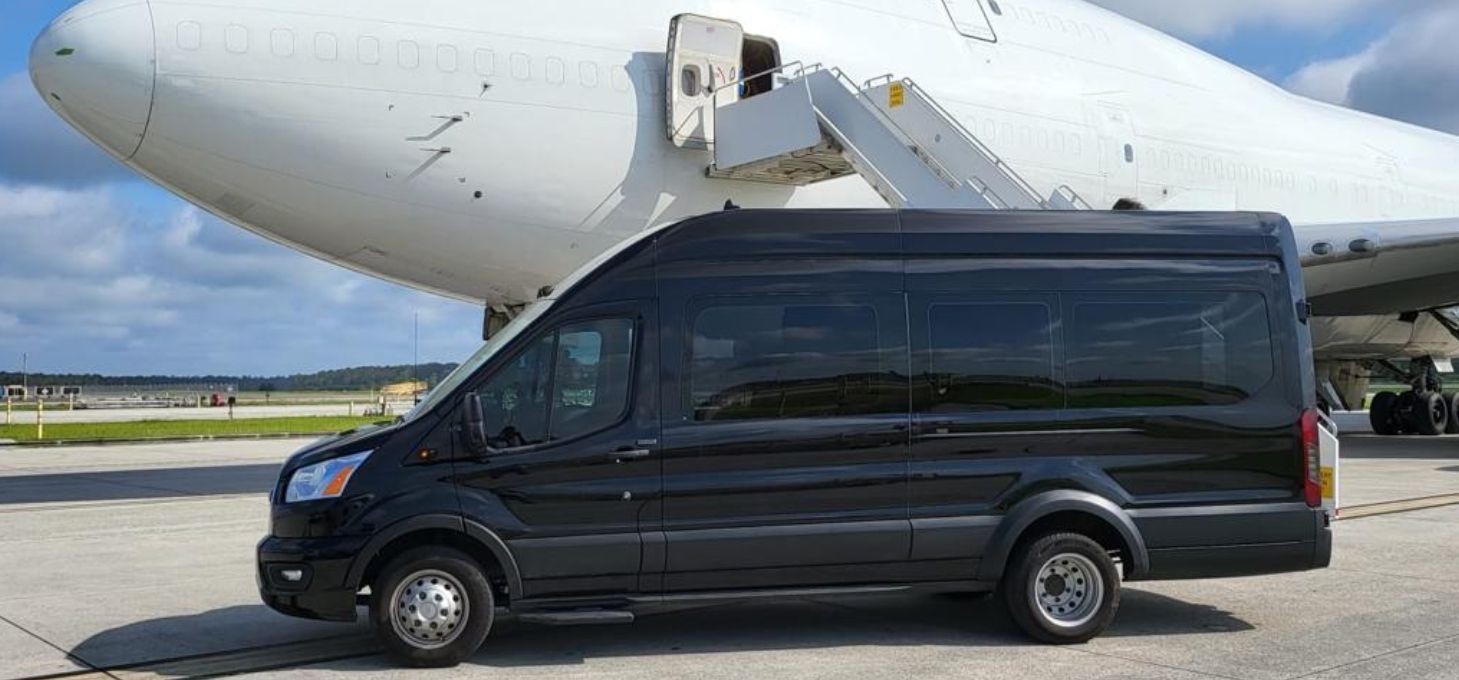 Black van parked on a tarmac next to a large white airplane.