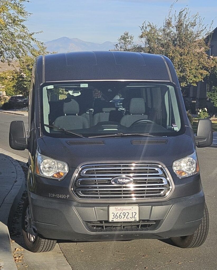 Dark gray Ford Transit van parked on a street with a mountain background.
