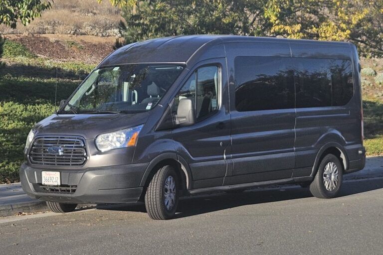 Dark gray passenger van parked on a road, with a grassy hillside in the background.
