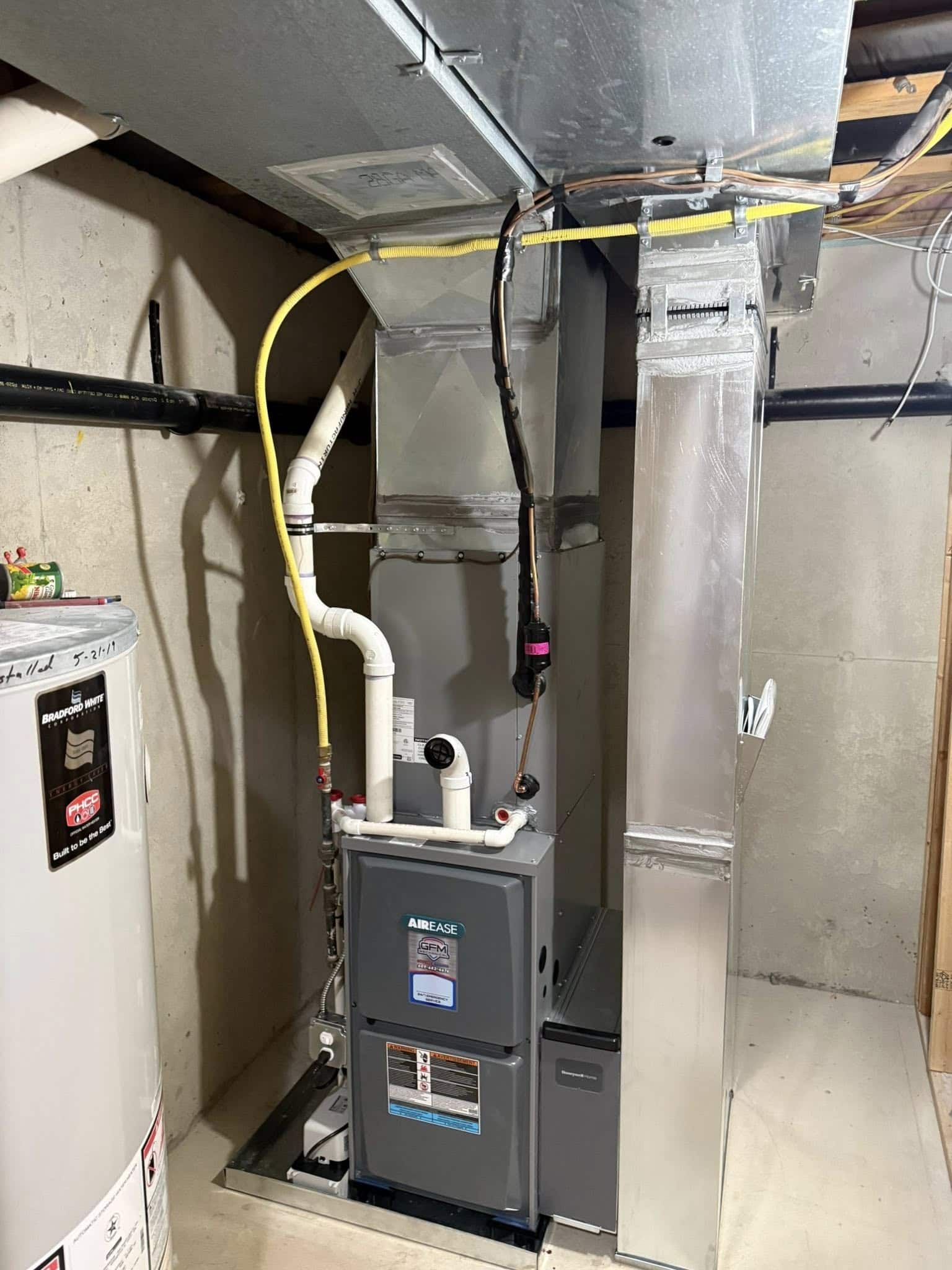 A gas furnace is sitting in a basement next to a water heater.