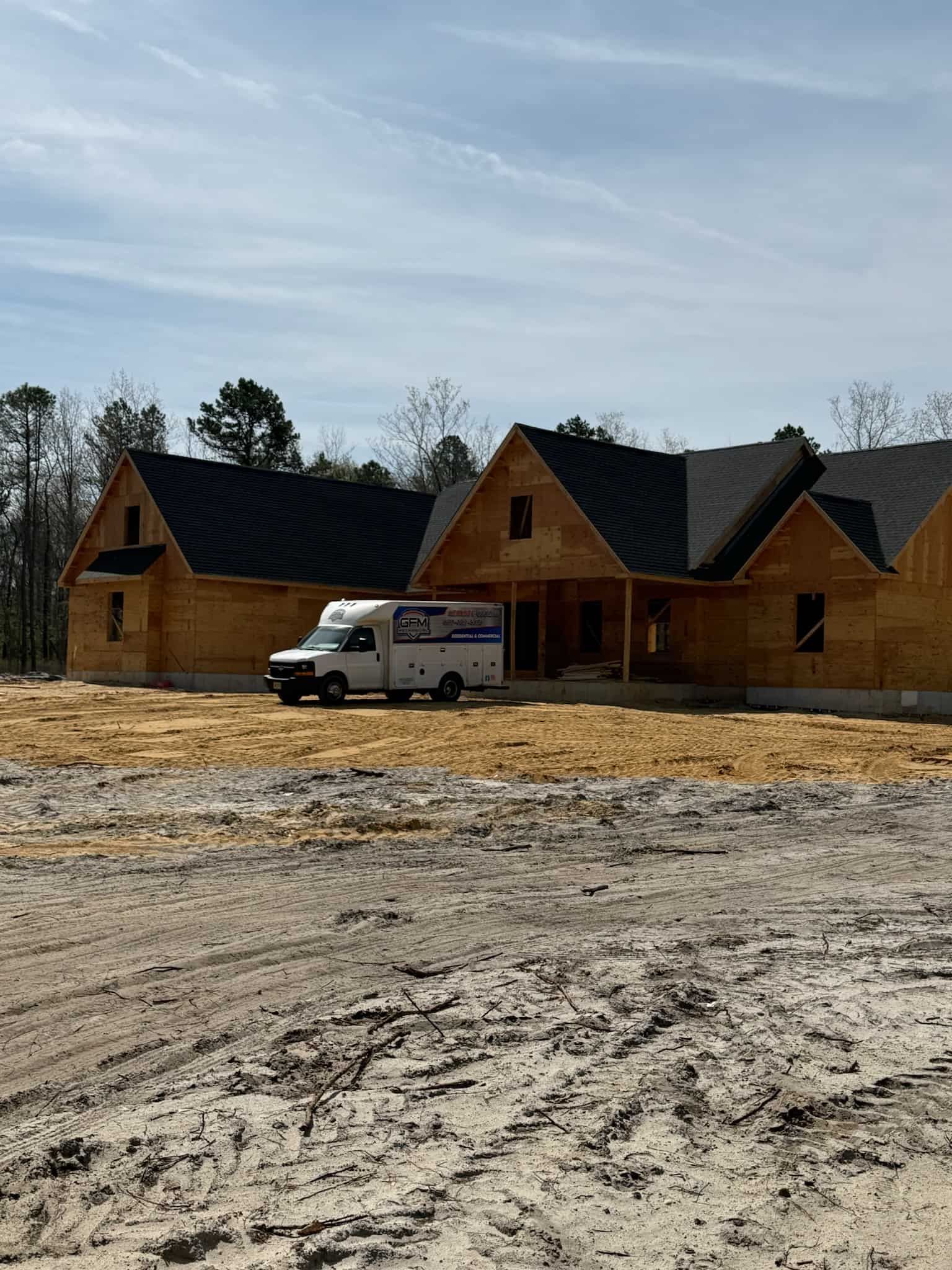 A white van is parked in front of a wooden house under construction.
