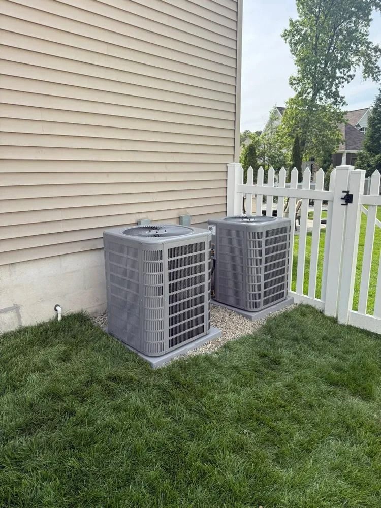 Two air conditioners are sitting on the side of a house next to a white picket fence.