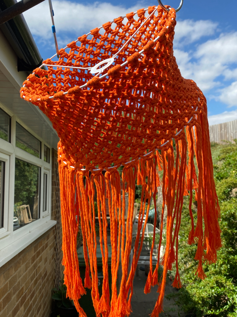 Lampshade made from bright orange, 4mm  cotton cord. Hanging outside, swinging in the breeze.