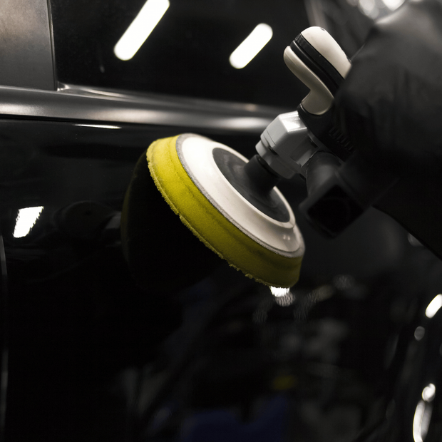 A person is polishing a car with a yellow pad