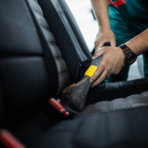 A man is cleaning the back seat of a car with a vacuum cleaner.