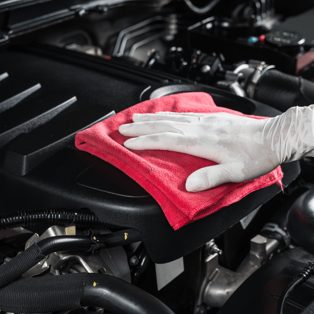 A person is cleaning a car engine with a red cloth.