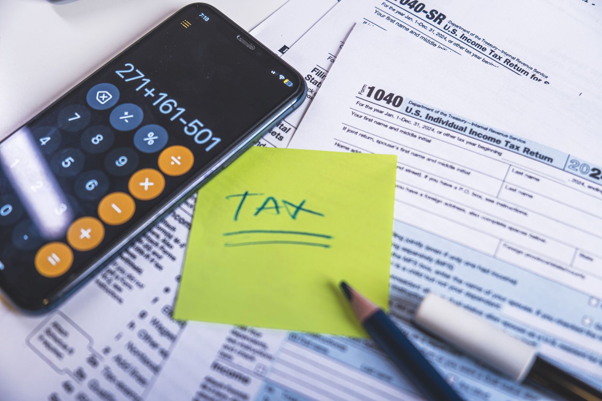 A calculator is sitting on top of a tax form next to a sticky note that says tax.