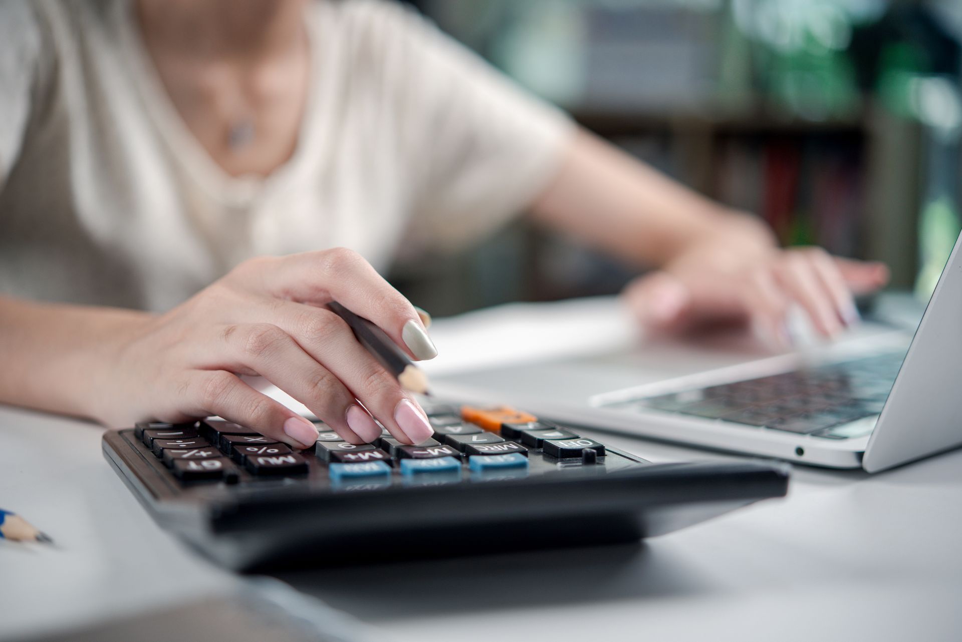 A woman is using a calculator in front of a laptop computer.