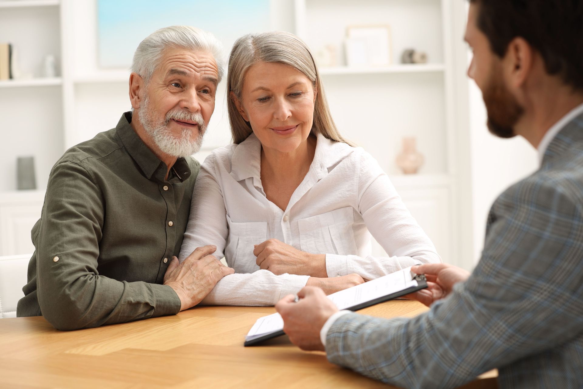 An elderly couple is sitting at a table talking to a man.