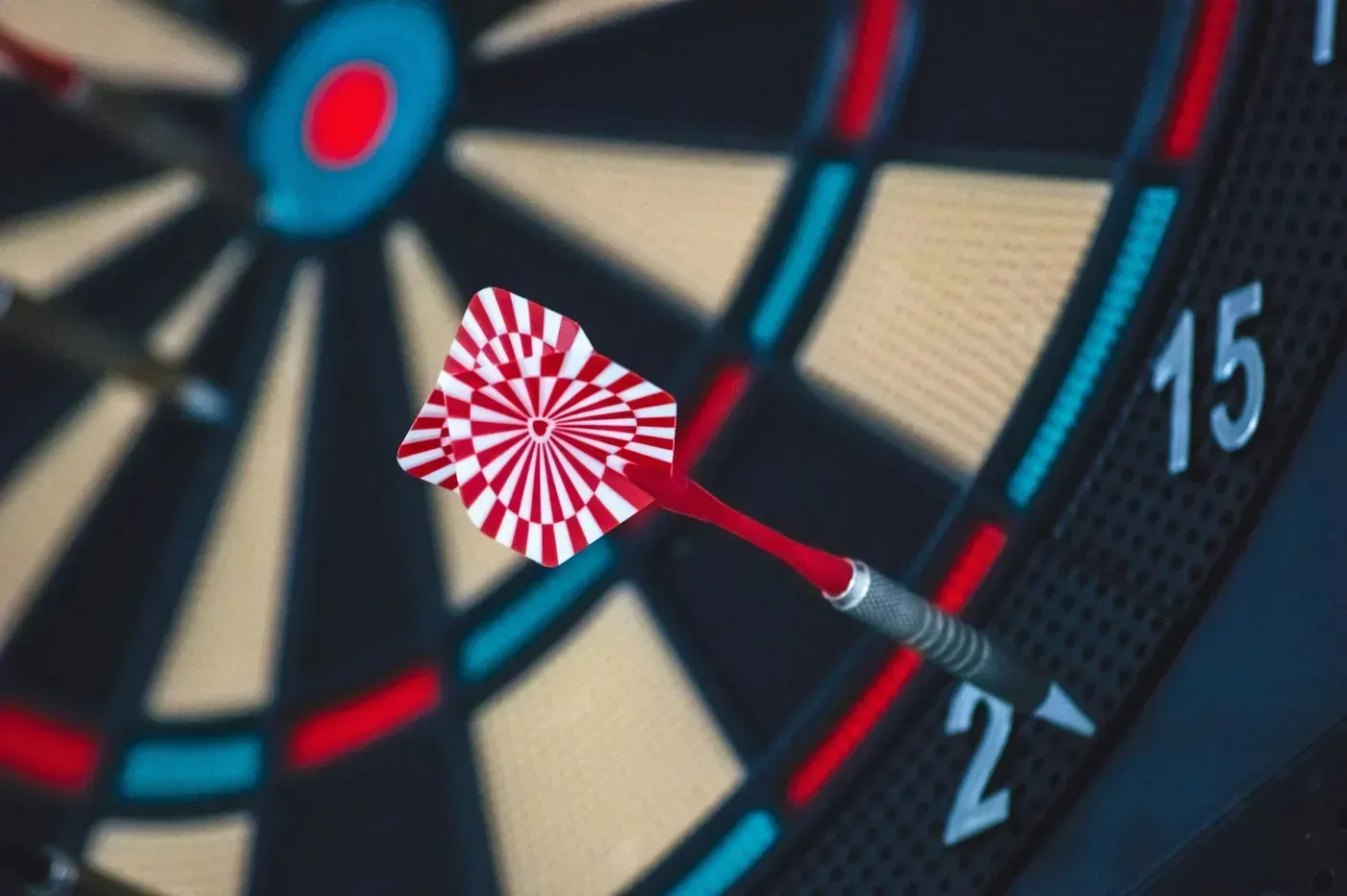 Dart in a dartboard, bullseye. Red, white dart, blue, black, and white board with score markings.