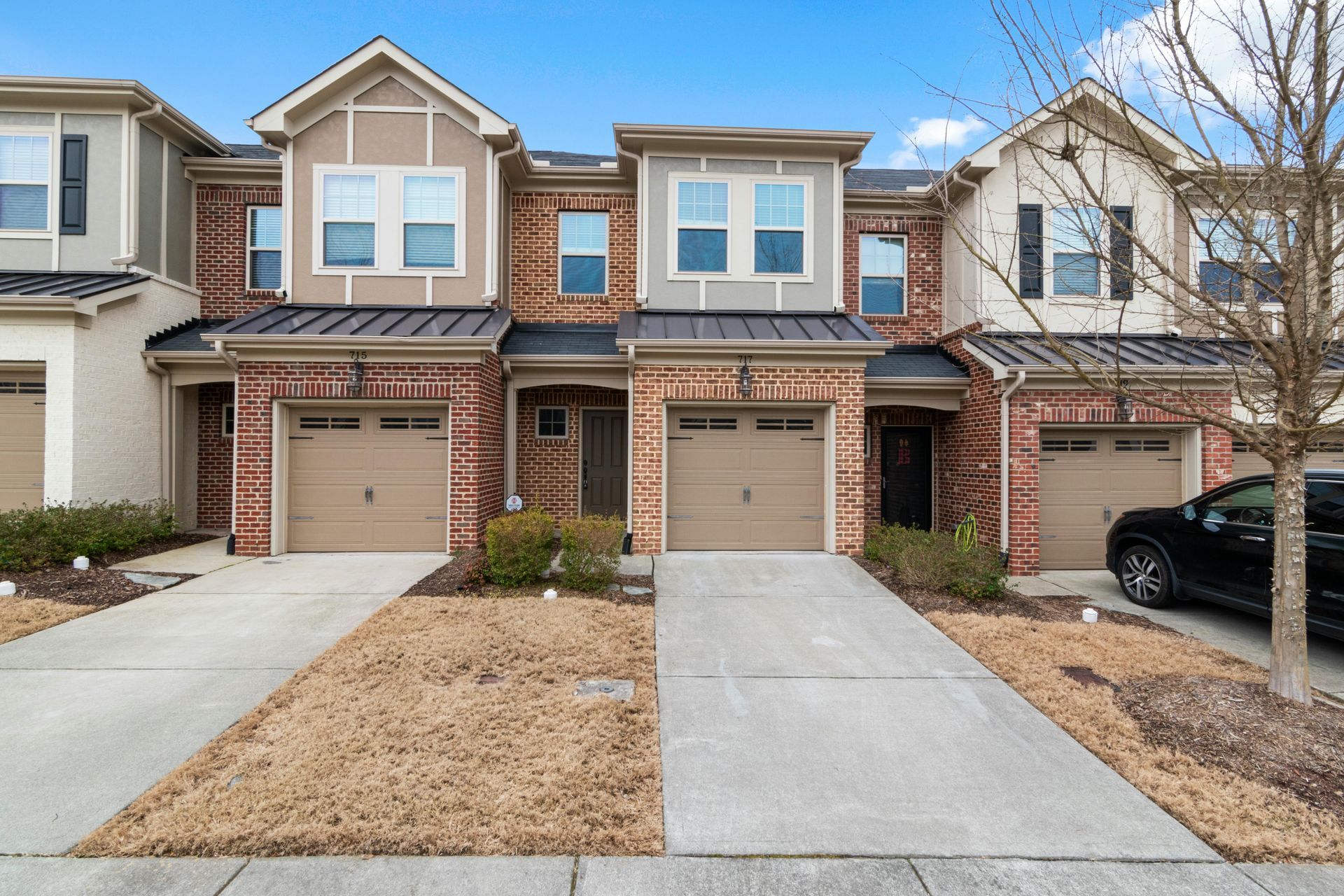Townhouses with brick exteriors, tan garage doors, and driveways, on a sunny day.