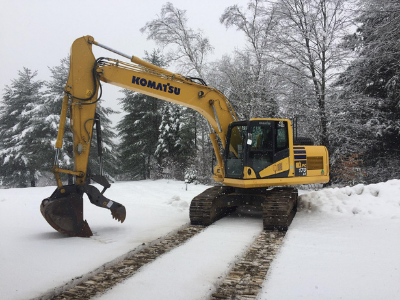 A yellow Komatsu excavator with a mechanical thumb attachment parked in a snowy landscape.