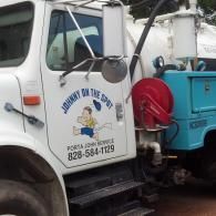 A white Johnny on the Spot porta-john service truck features a logo of a cartoon character and phone number 828-584-1129.