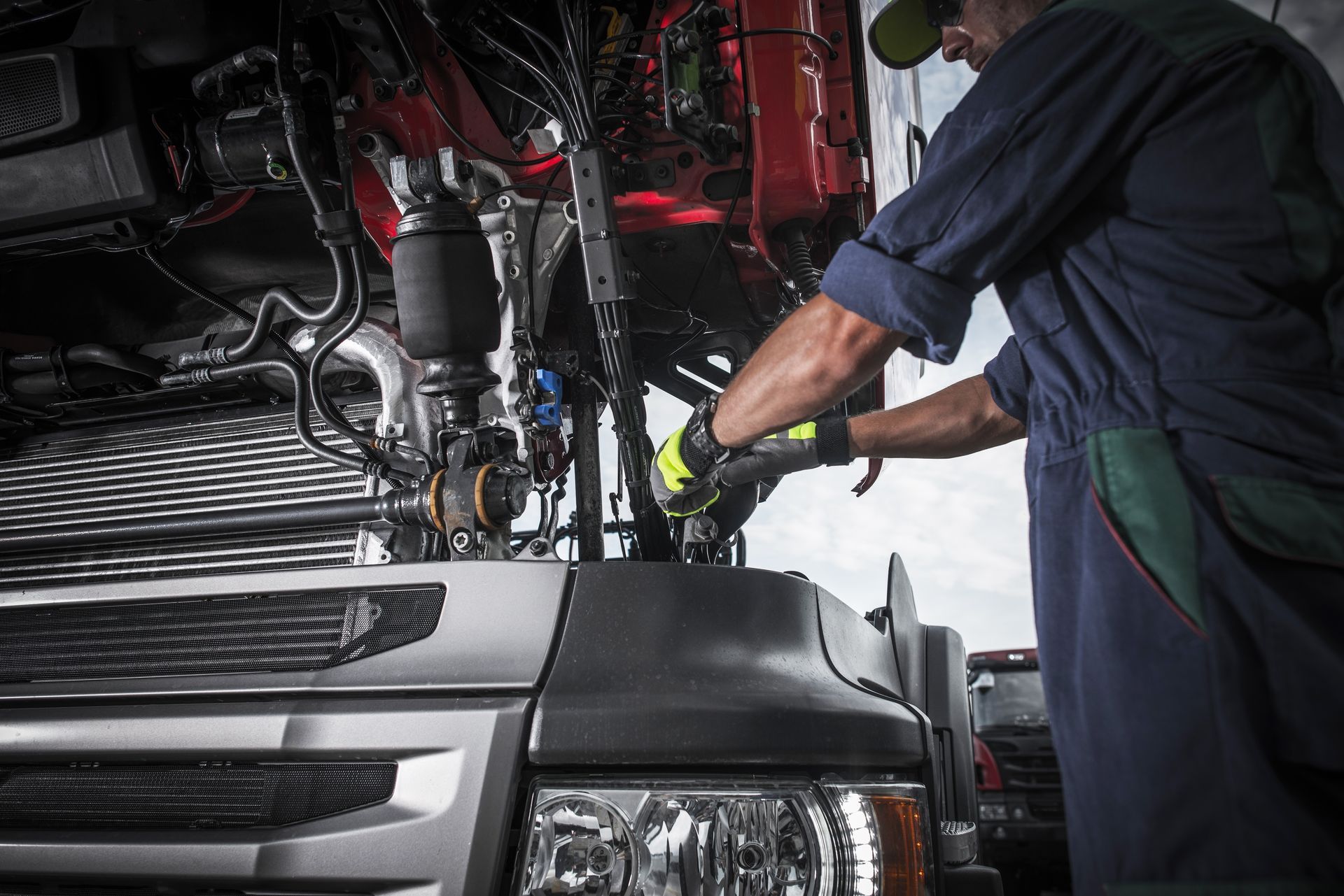 Mechanic in blue overalls performing expert commercial truck repair on a heavy-duty engine. Mechanic in blue overalls performing expert commercial truck repair on a heavy-duty engine.
