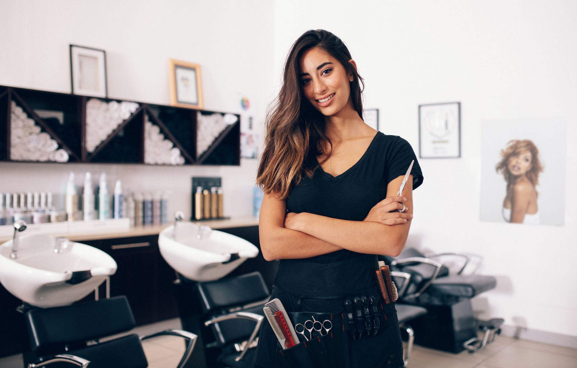 A woman is standing in a hair salon with her arms crossed.