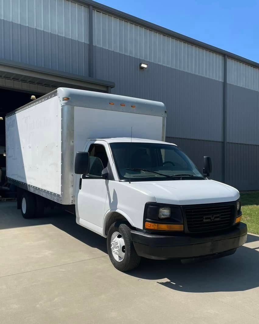 White box truck parked in front of a gray industrial building.