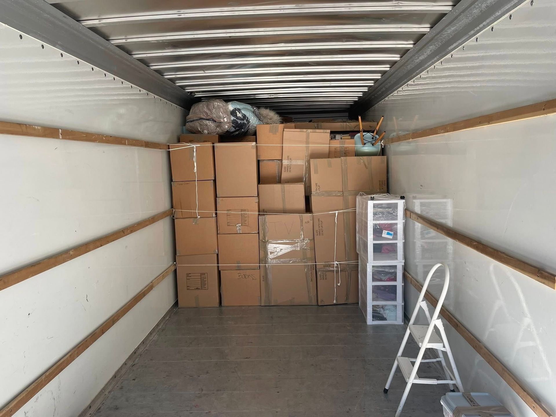 Interior of a moving truck filled with cardboard boxes, plastic drawers, and a ladder.