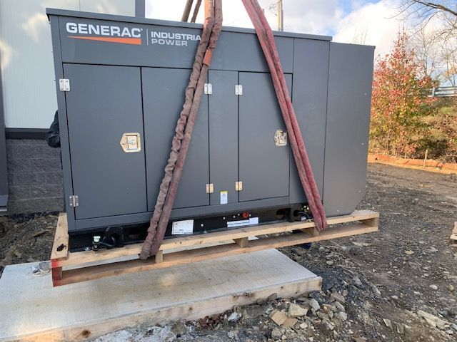 A generator is being lifted by a crane on a wooden pallet.