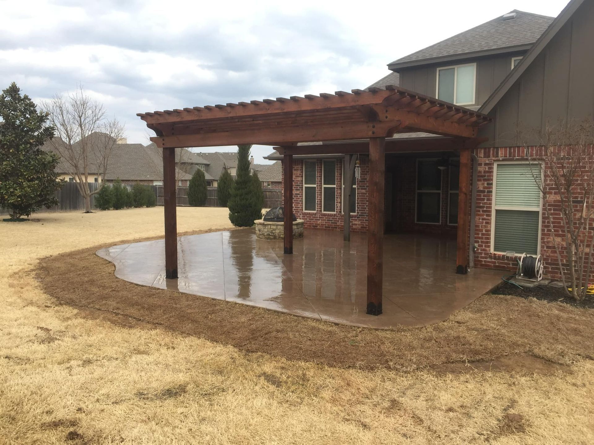 A patio with a pergola and a brick house in the background
