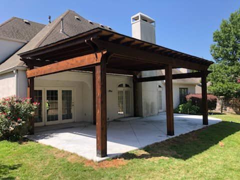 A large wooden pergola is in the backyard of a house.