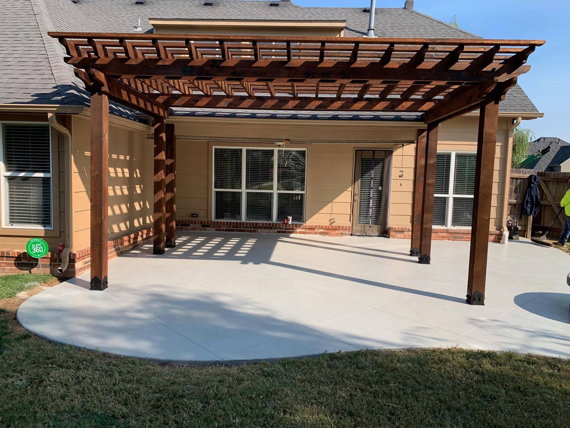 A wooden pergola is sitting on top of a concrete patio in front of a house.
