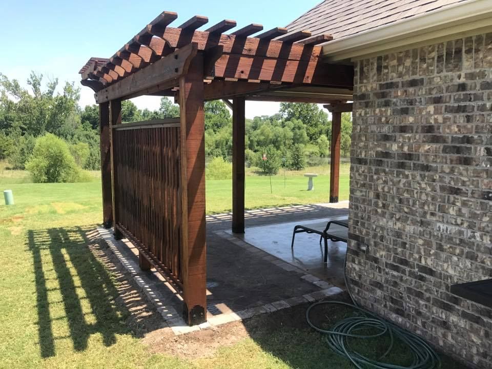 A wooden pergola is attached to the side of a brick house
