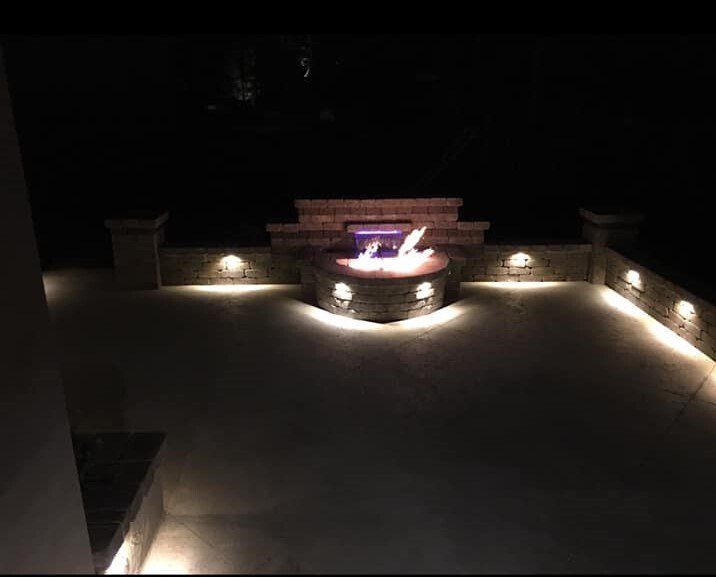 A fire pit is lit up at night on a patio.