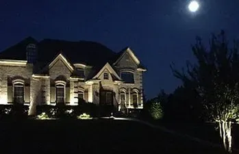 A large house is lit up at night with a full moon in the background.