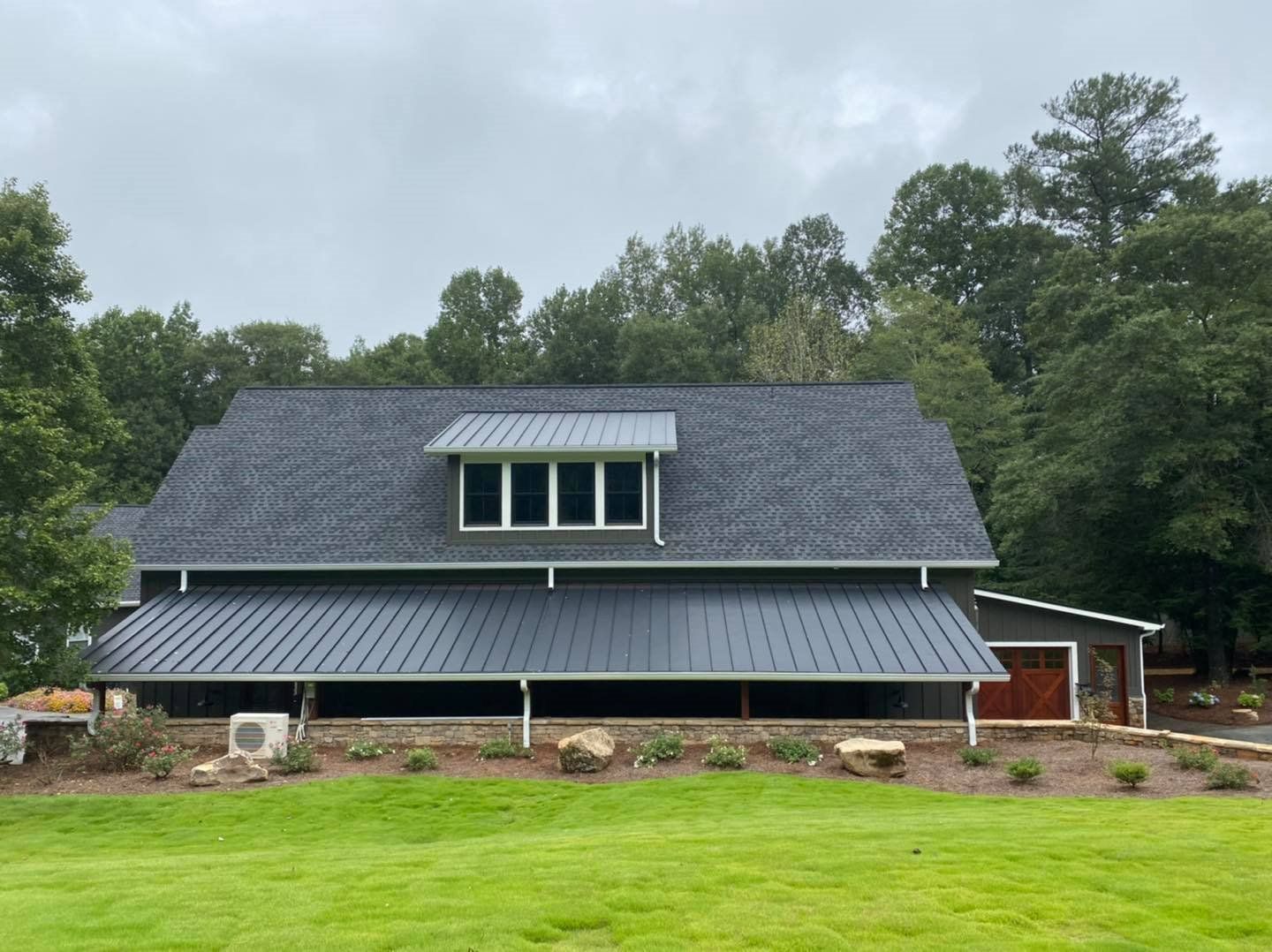 A large house with a gray roof is sitting on top of a lush green field.