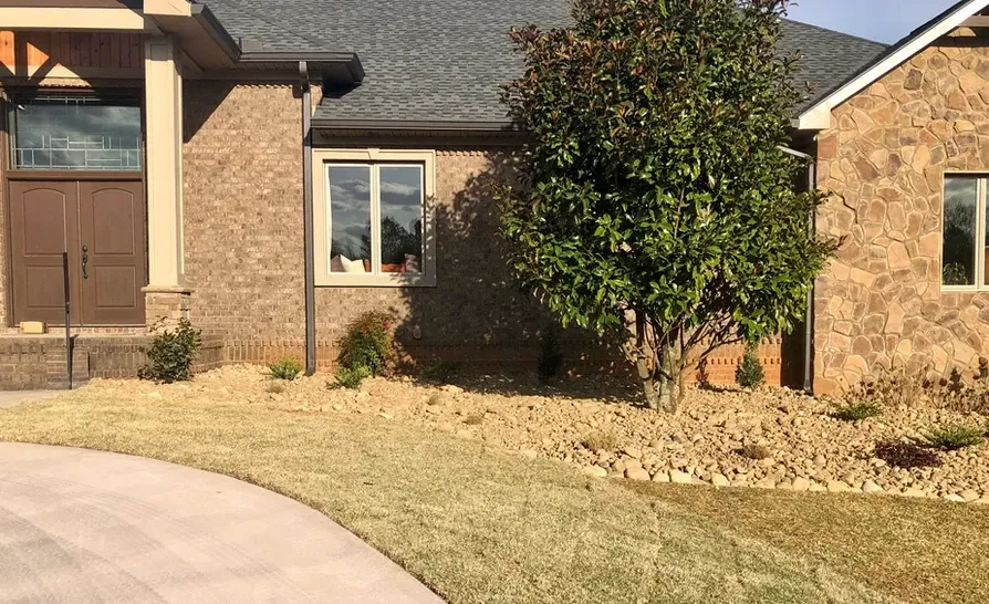 A brick house with a driveway and a tree in front of it.