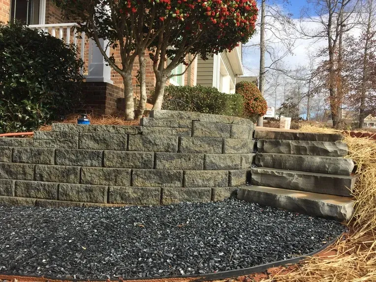 A stone wall with stairs and gravel in front of a house.