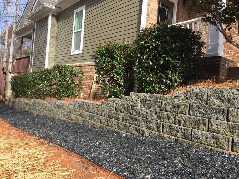 A house with a stone wall and a walkway in front of it.