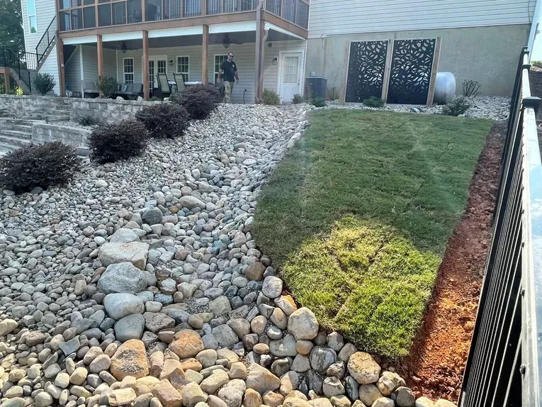 A house with a fence and a rock garden in front of it.