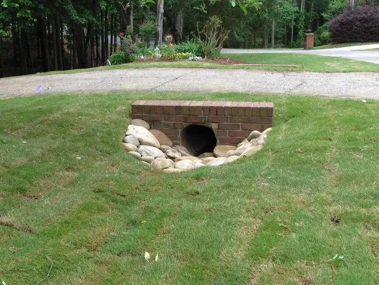 A brick bridge over a drain in the grass.