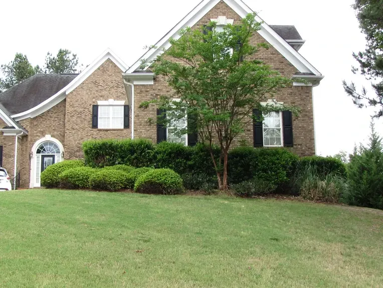 A large brick house with black shutters and a lush green lawn.