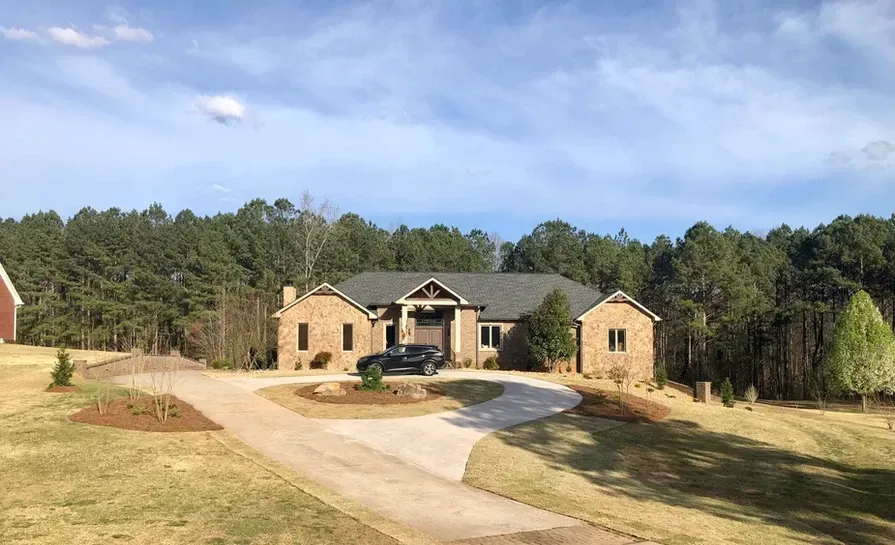 A large brick house with a car parked in front of it is surrounded by trees.