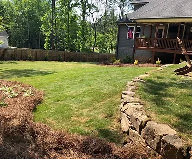 A large lawn with a stone wall in front of a house.