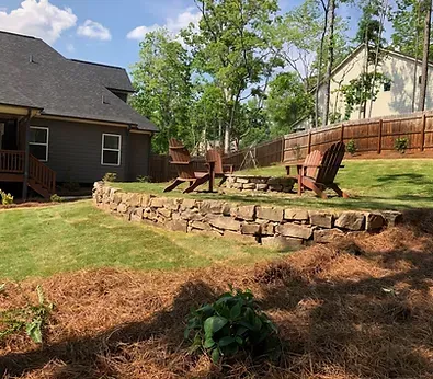 A lawn with a stone wall and chairs in front of a house.