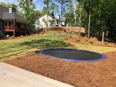 A trampoline is in the middle of a lush green yard in front of a house.