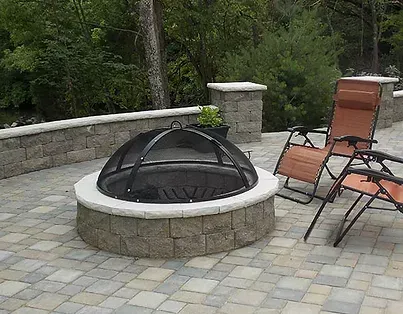 A fire pit is sitting on a patio next to two chairs.