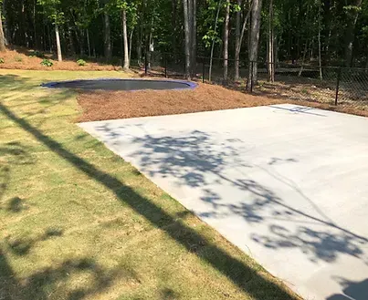 A concrete driveway with a fence and trees in the background.