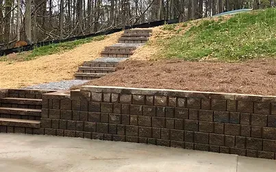 A stone wall with stairs leading up to a grassy hill.