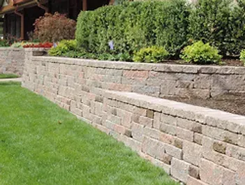 A stone wall surrounds a lush green lawn in front of a house.