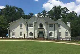 A large white house is sitting on top of a lush green field.