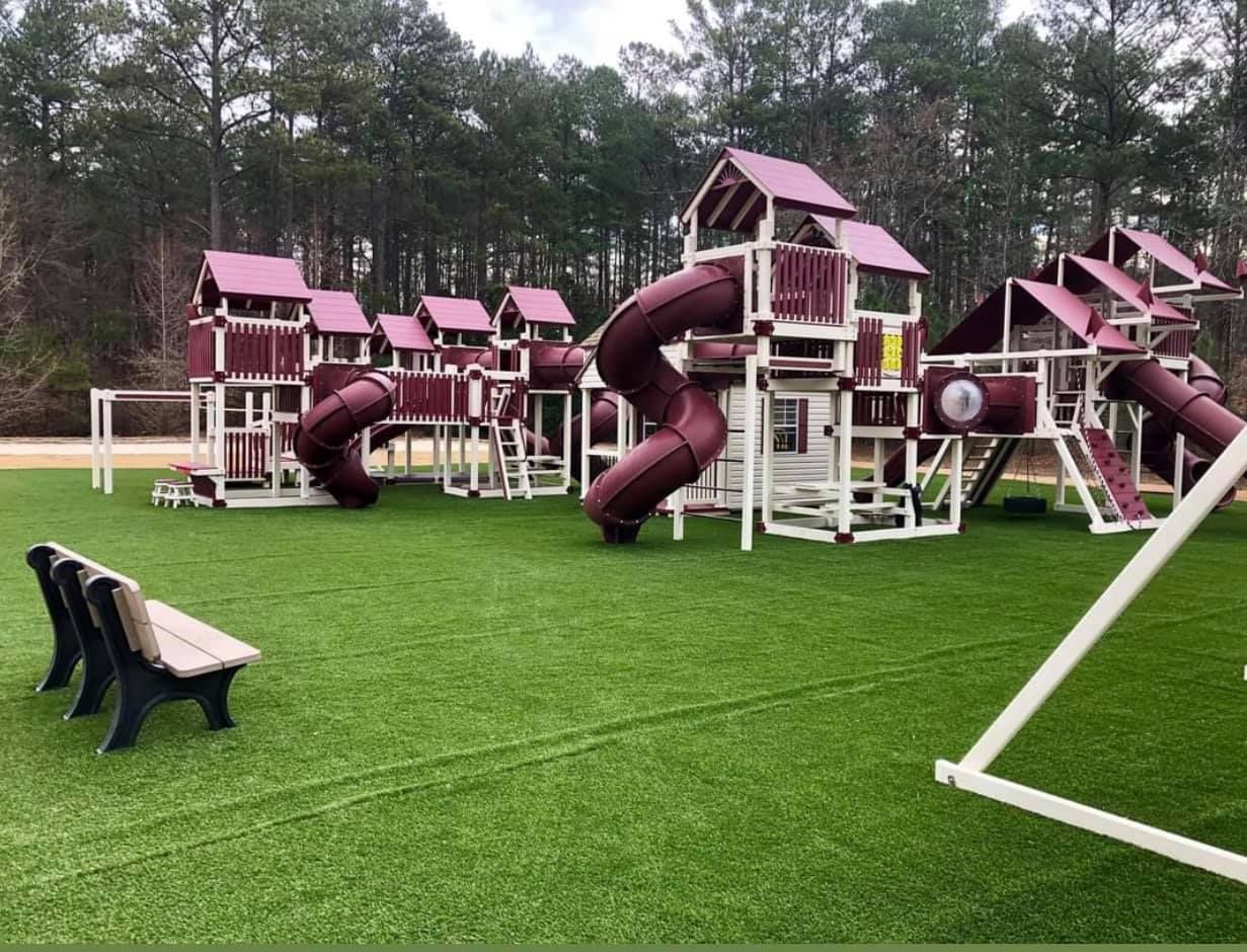 A large playground with a bench in the foreground and trees in the background.