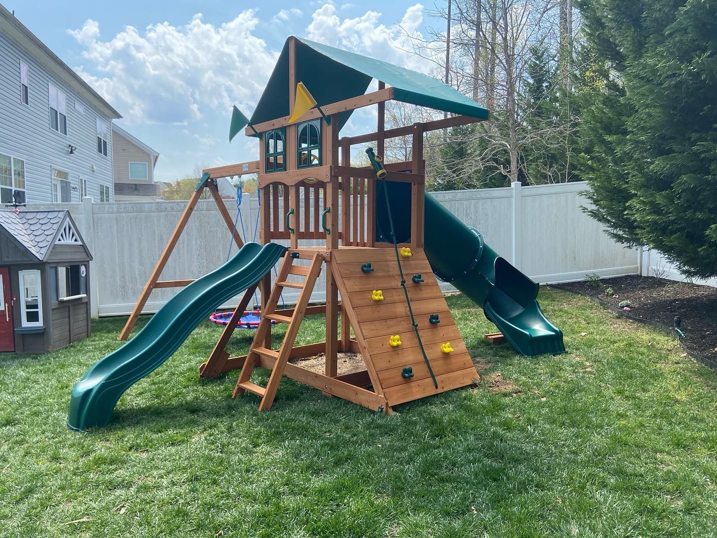 A wooden playground set with a slide and climbing wall in a backyard.