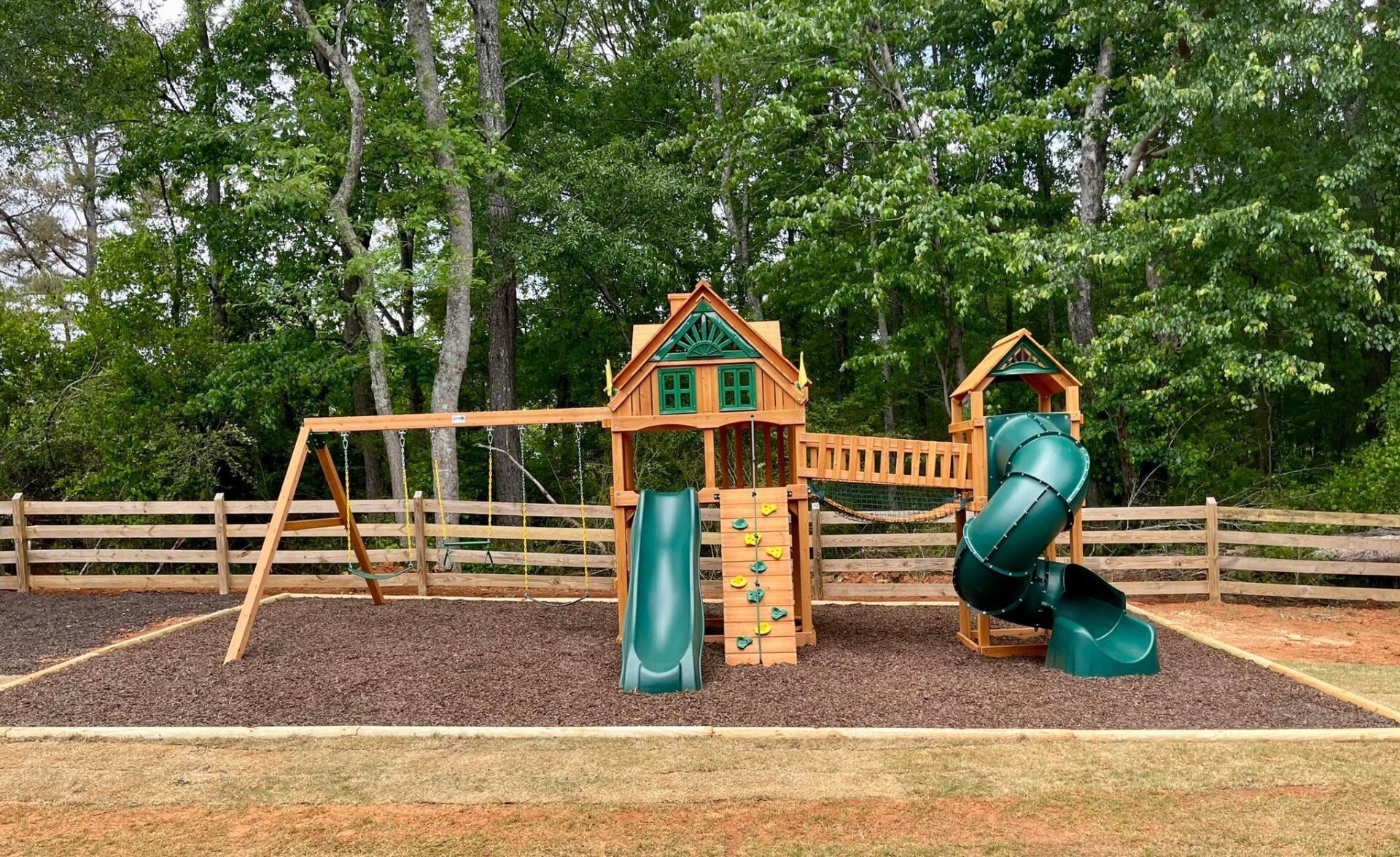 A wooden playground set with a green slide and swings in a yard.