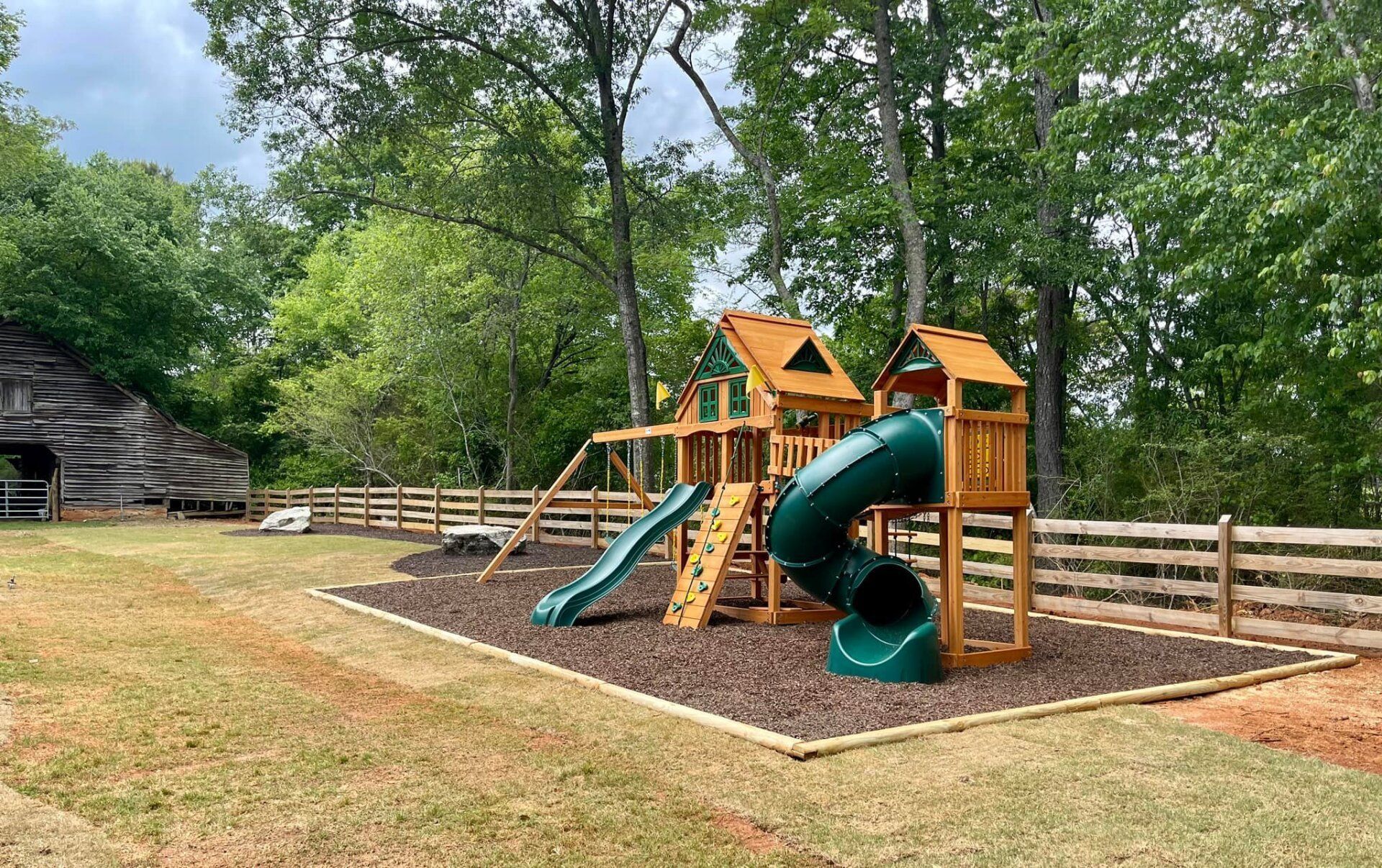 A wooden playground with a green slide and a wooden fence in the background.