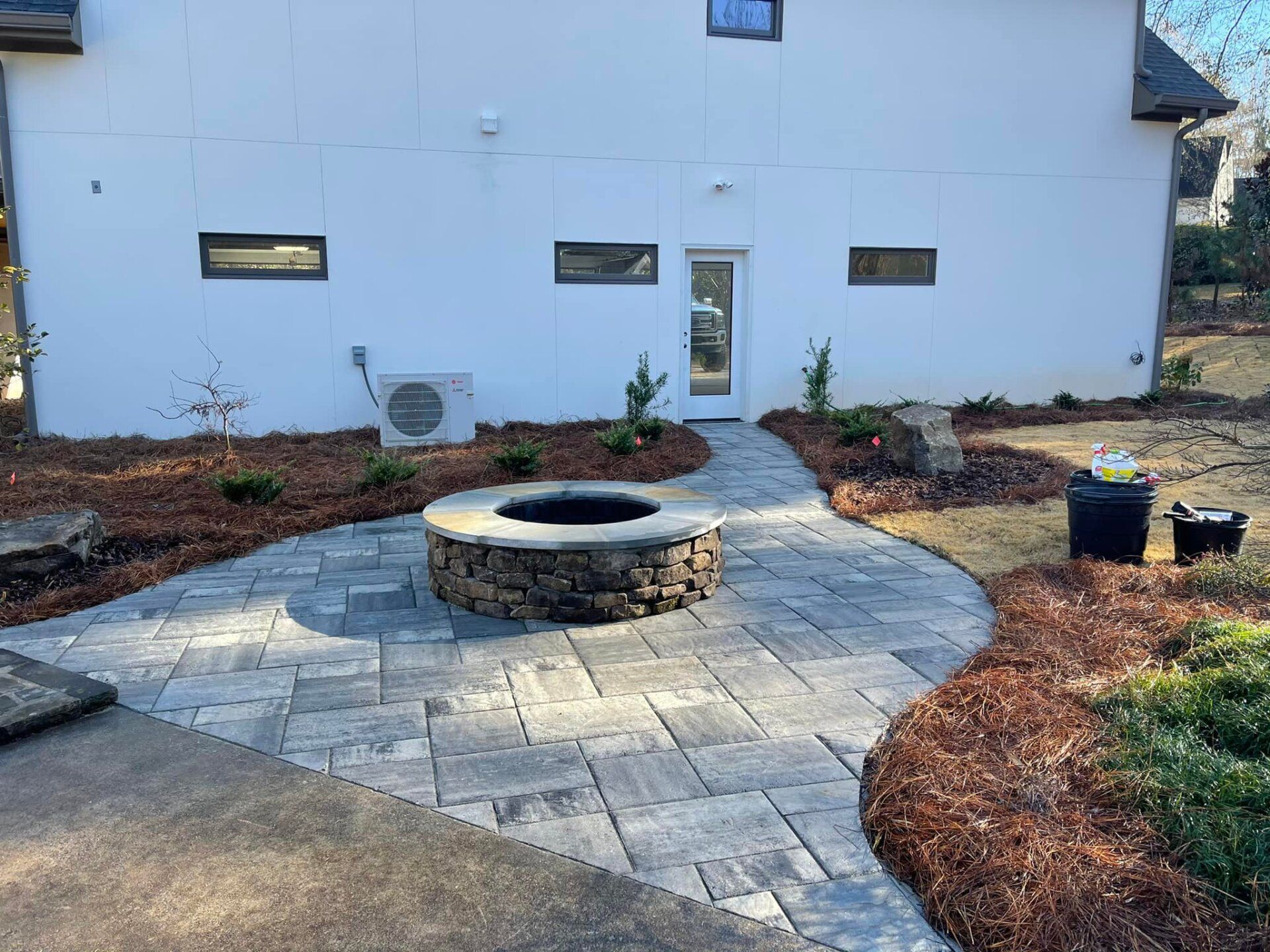 A fire pit is in the middle of a patio in front of a house.